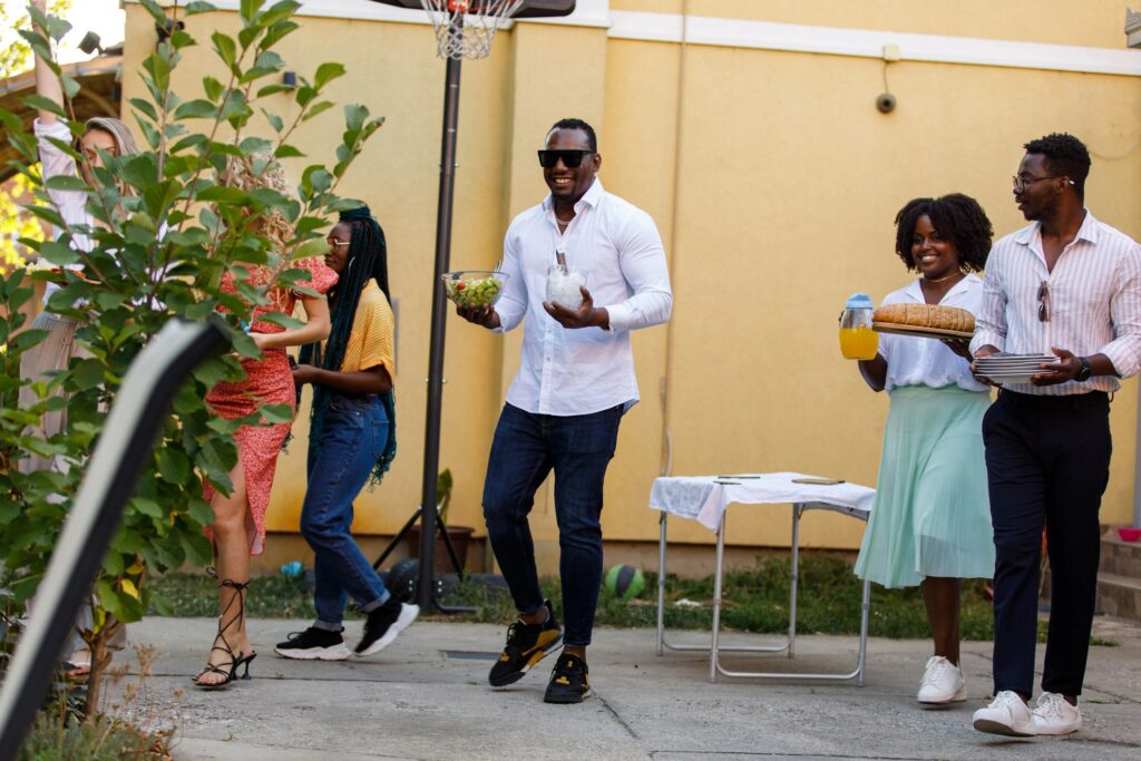 Group of friends carrying food, drinks and cutlery to the table during a dinner party